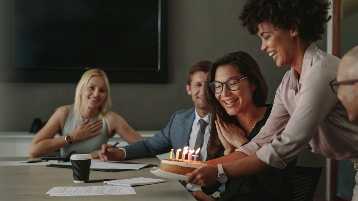 woman bringing in birthday cake to colleague