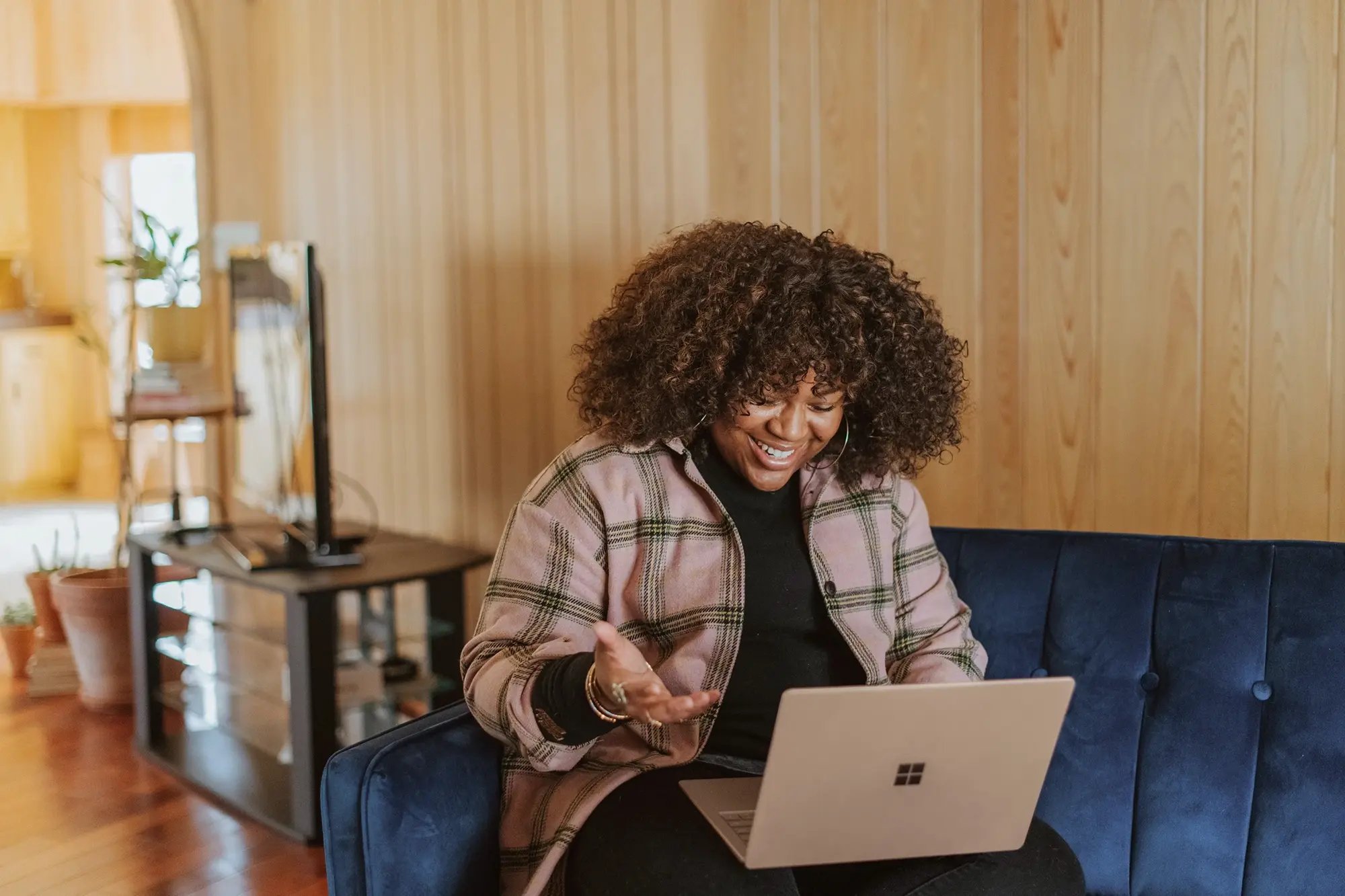 Mixed race women sits on a sofa looking at a laptop. She is smiling and gesturing as if having a conversion